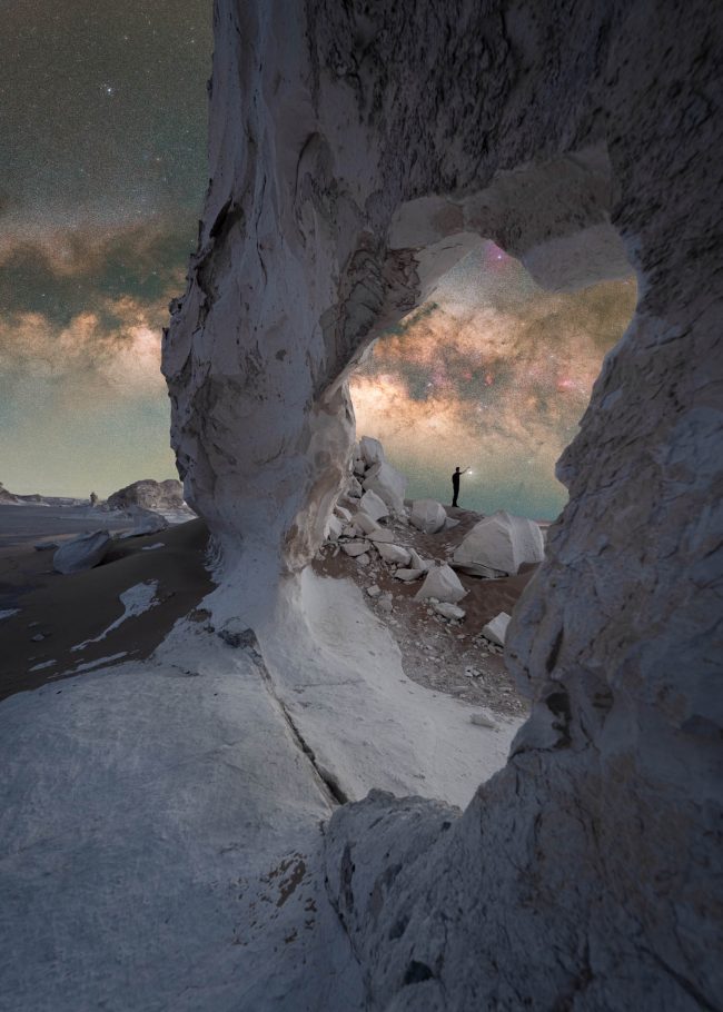 银河出现在一个不规则的岩石拱门中，远处有摘星辰的人。