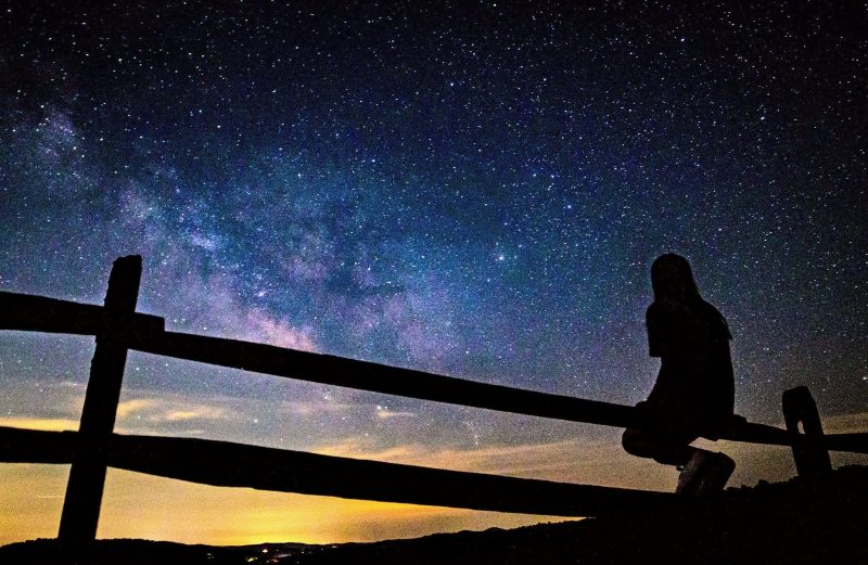 孩子坐在栏杆上，看着银河。作者：Thomas Frazier)