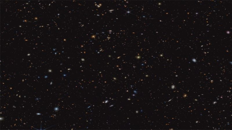 45,000 个婴儿星系：黑色背景上的小螺旋和不规则形状的斑点（白色、蓝色、黄色和橙色）。图像来源：NASA